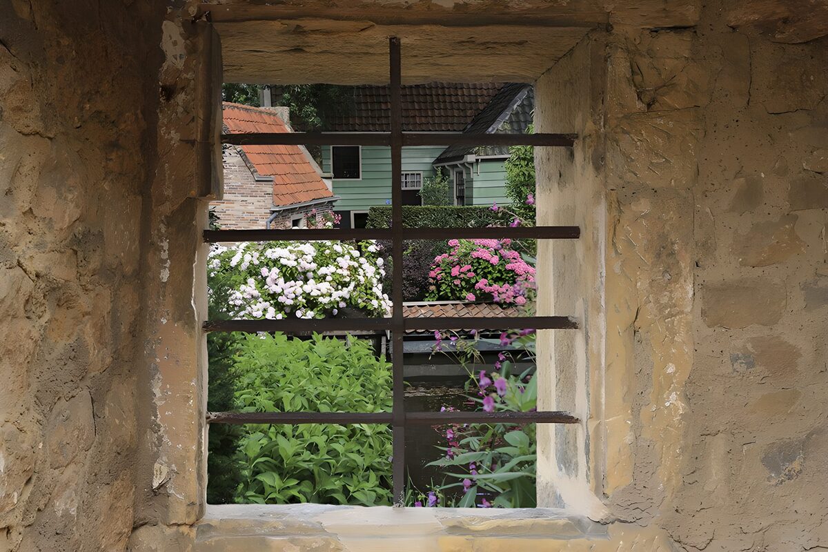 TPDE13474: durch das Fenstergitter sieht man die Holzhäuser von einem Dorf