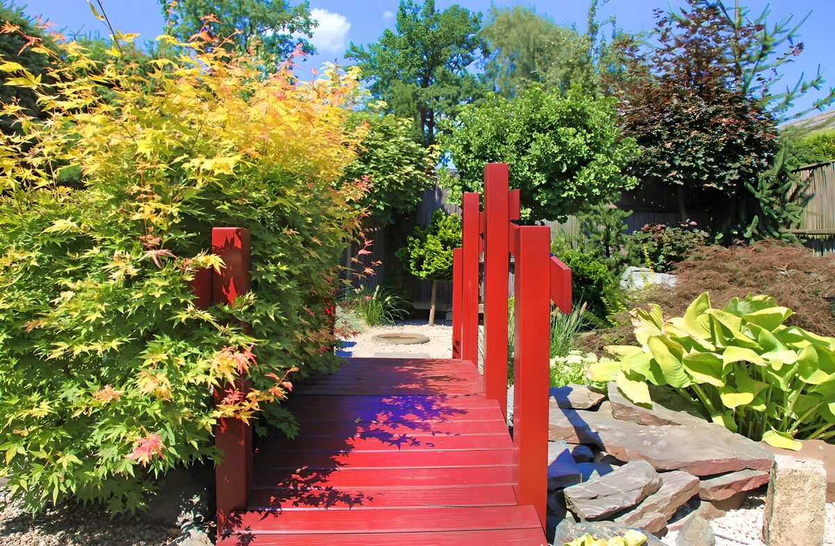 Rote Brücke über einen Bach inmitter der üppigen Natur in einem japanischen Garten