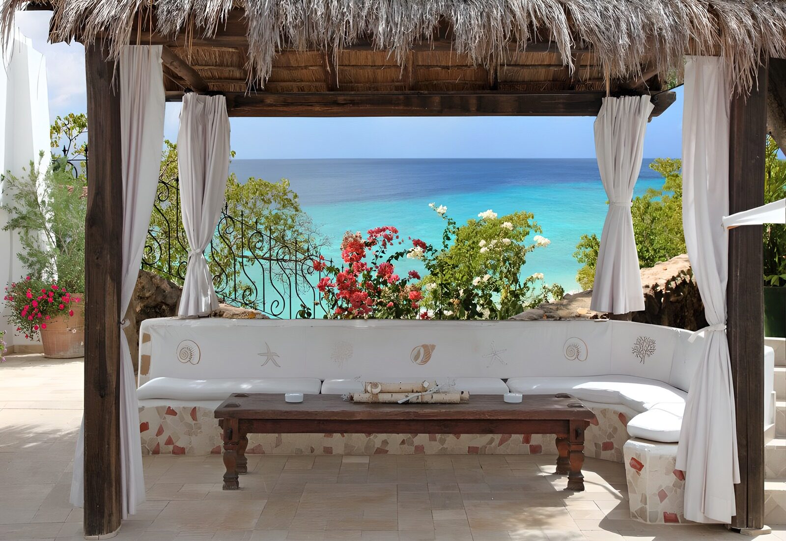TPDE14839: schattige Sitzecke mit roten und weißen Blüten mediterraner Pflanzen und das meer im Hintergrund