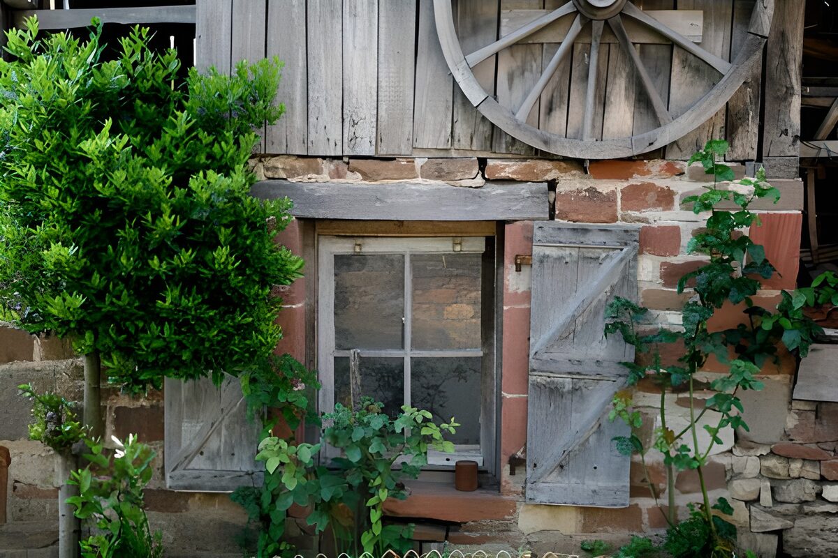 Alter französischer Bauernhof mit einem alten Rad, Efeu und einem Baum und vergraute Fensterläden