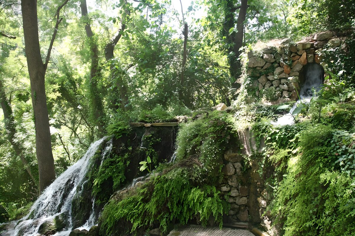 Mauer aus Kieselsteinen mit einem kleinen Wasserfall bewachsen mit unterschiedlichen Pflanzen