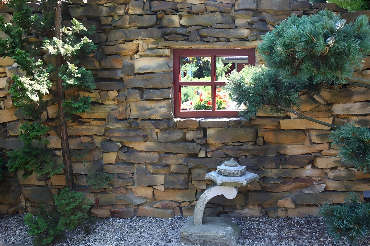 Blick auf eine Mauer aus Lavasteinen und ein Fenster mit Blick  in einen Innengarten gucken kann